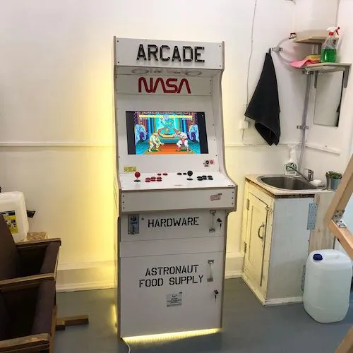 A photo of a plywood arcade machine that is painted white and emblazoned with the NASA livery.