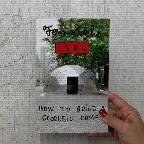 A photo of a hand holding a copy of the zine How to Build a Geodesic dome.