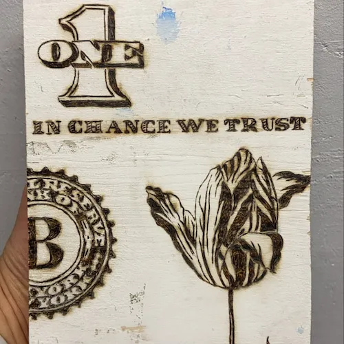 A photo of plywood painted white with 'in chance we trust' burned onto it.