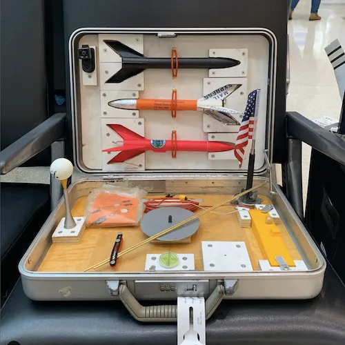 A photo of an open metal suitcase with three model rockets mounted inside.