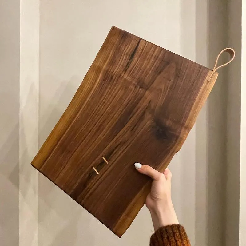 A photo of a hand holding a chopping board up against a wall.