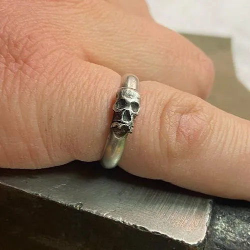 A photo a silver skull ring worn on a pinkie finger.