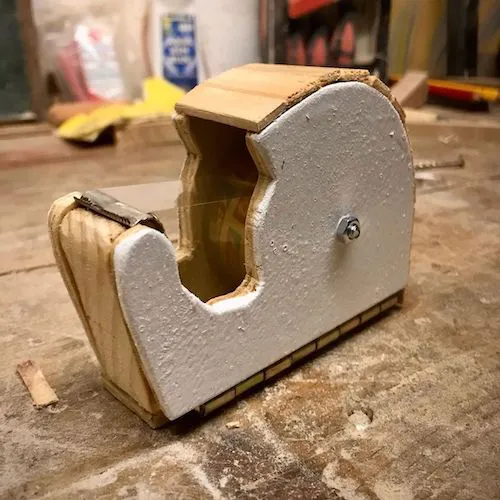A photo of a small plywood tape dispenser that has been painted white.