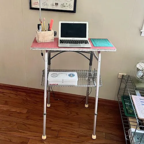 A photo of a repuporsed zimmer frame that has been converted into a standing desk with a shelf.